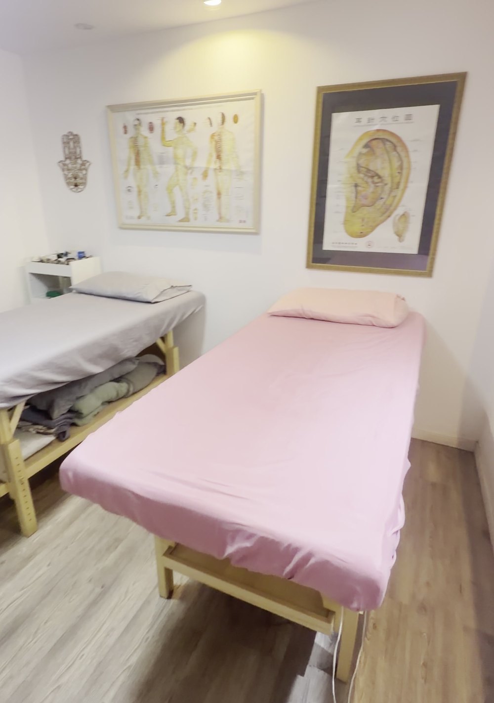 A sala de acupuntura do consultório: duas macas com lençóis limpos e os mapas de pontos de acupuntura emoldurados na parede.